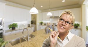 Attractive Daydreaming Woman with Pencil Inside Beautiful Custom Kitchen.